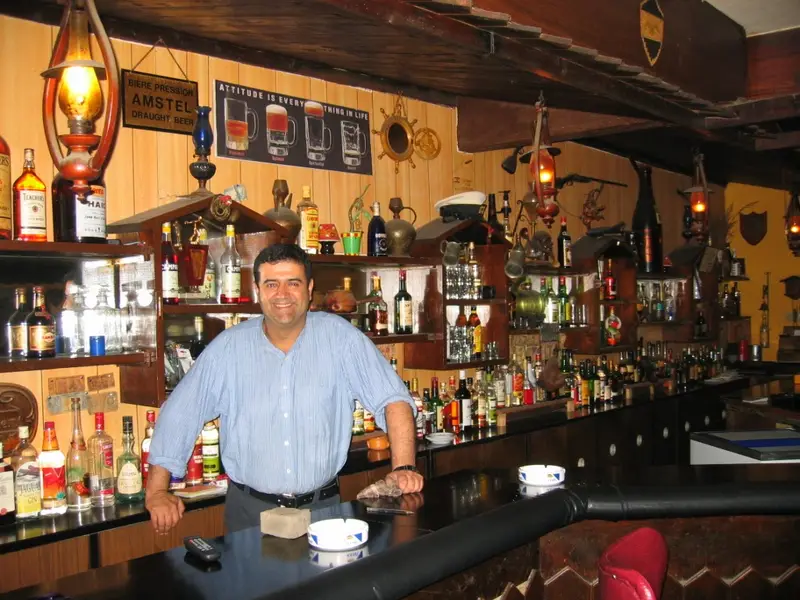 Andre, the longtime owner of Captain’s Cabin, standing behind the bar in front of the bottle shelves