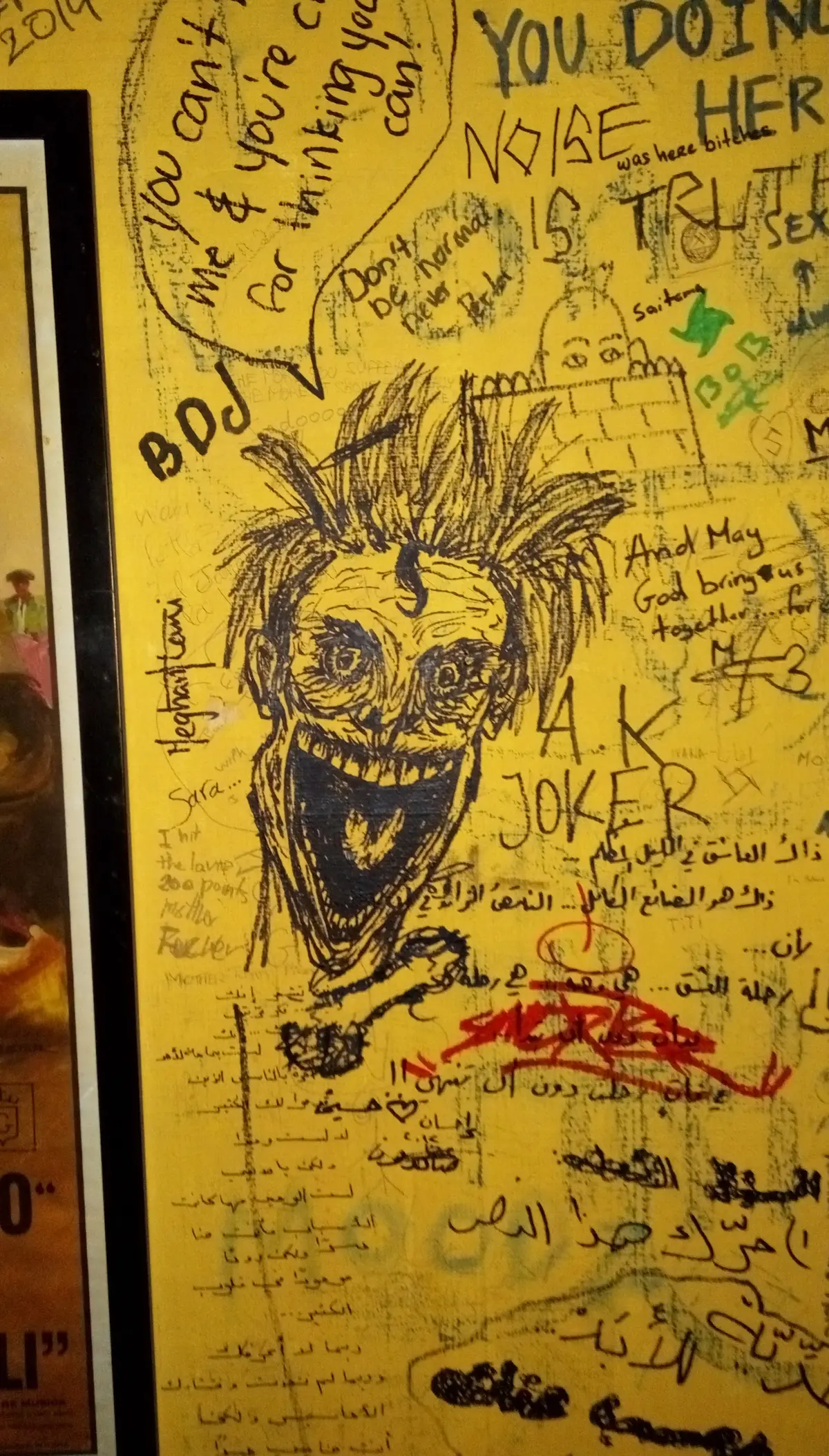 A grinning face drawn in pen on the bar’s yellow wall, surrounded by messages in English and Arabic