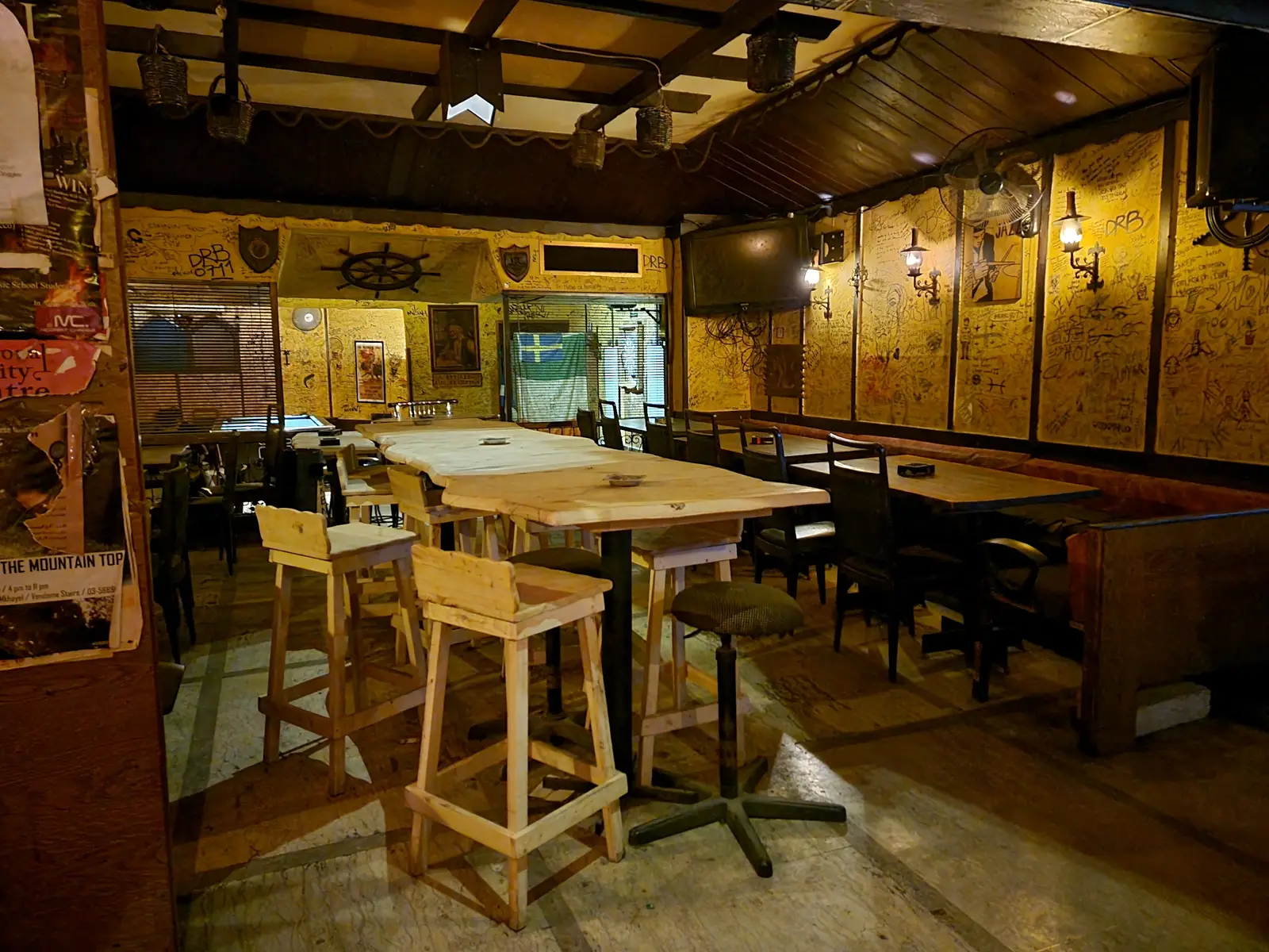 The main room at Captain's Cabin: wood-paneled walls covered in customers' signatures, a ship's wheel above the bar, wooden stools and low amber lighting